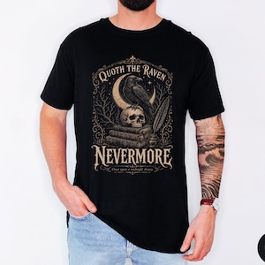 Puede incluir: Una camiseta negra con un estampado gr&aacute;fico de un cuervo posado sobre una calavera encima de una pila de libros, con una luna creciente y una pluma. El texto dice QUOTH THE RAVEN NEVERMORE y Once upon a midnight dreary en letra decorativa.