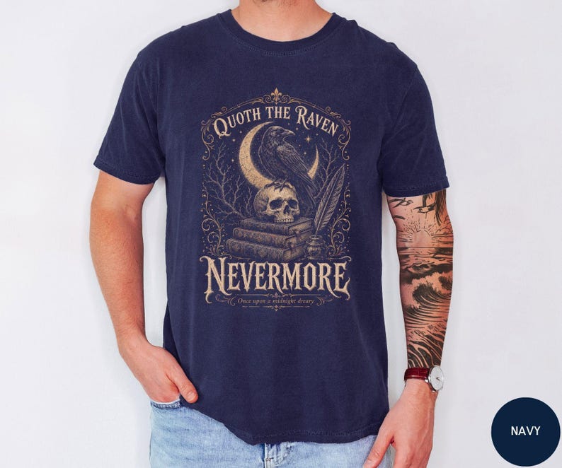 Puede incluir: Una camiseta azul marino con un estampado gr&aacute;fico de un cuervo posado sobre una calavera encima de una pila de libros, con una luna creciente, una pluma y el texto "QUOTH THE RAVEN NEVERMORE" y "Once upon a midnight dreary" en fuente beige.