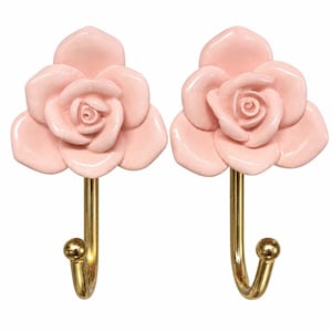 May include: A pair of wall hooks featuring a three-dimensional light pink rose flower head made of a smooth material, attached to a polished gold-toned metal hook with a small spherical tip at the end of the curved arm for hanging items.