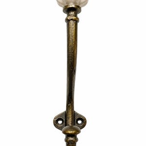 May include: A wall-mounted coat hook featuring a textured, antique brass-finished metal arm and a base with two screw holes. The top of the hook is capped with a smooth, white, pumpkin-shaped ceramic knob, providing a contrast to the dark metal.