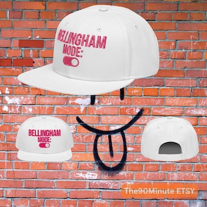 May include: White baseball cap with the text "Bellingham Mode:" in pink embroidery. The cap features a flat brim and an adjustable snapback closure. The design includes a pink toggle graphic.