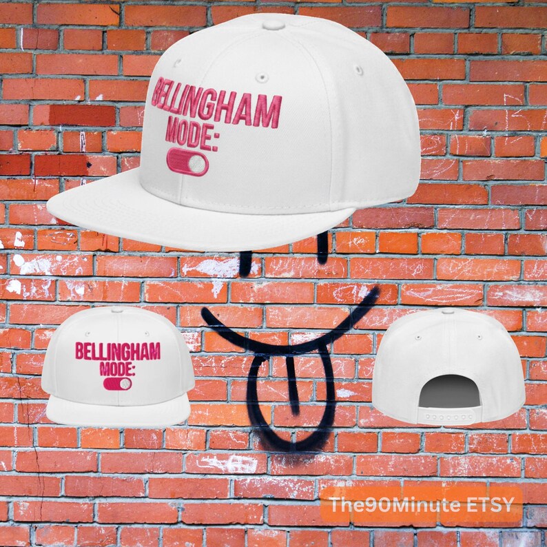 May include: White baseball cap with the text "Bellingham Mode:" in pink embroidery. The cap features a flat brim and an adjustable snapback closure. The design includes a pink toggle graphic.