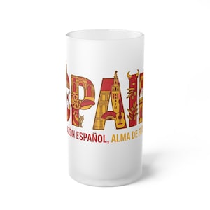 May include: A white frosted glass with the word "SPAIN" in red and yellow, featuring iconic Spanish imagery within the letters. The text "CORAZÓN ESPAÑOL, ALMA DE FUEGO" is printed below the word "SPAIN".