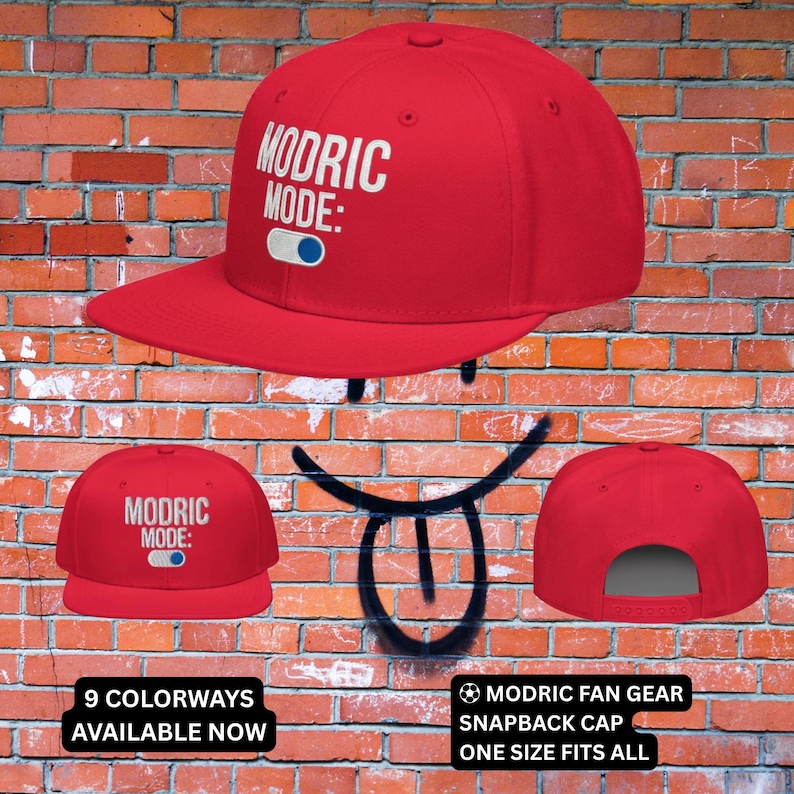May include: A red snapback cap with the text "MODRIC MODE:" in white. The cap has a flat brim and a gray underside. The image also shows the text "9 COLORWAYS AVAILABLE NOW" and "MODRIC FAN GEAR SNAPBACK CAP ONE SIZE FITS ALL".