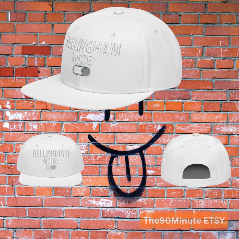 May include: A white baseball cap with a flat brim. The cap features the text "BELLINGHAM MODE:" in a light gray color, along with a graphic of a switch. The cap is set against a brick wall background.