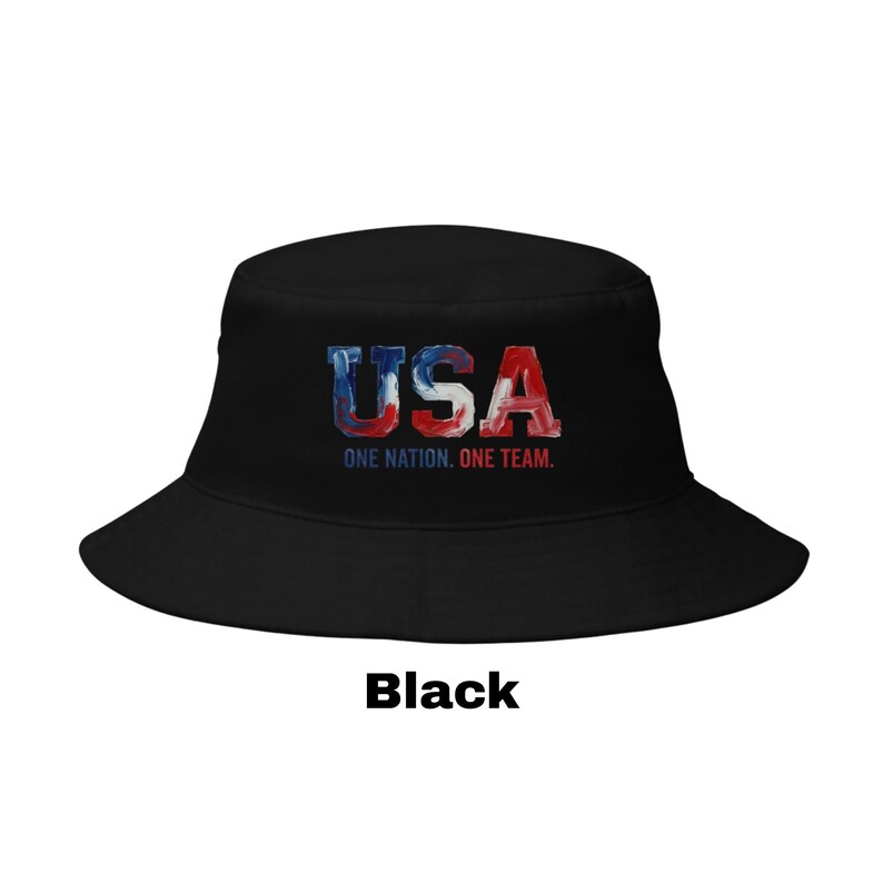 May include: Black bucket hat featuring the word "USA" in red, white, and blue, with the text "ONE NATION. ONE TEAM." The hat has a wide brim and a classic design.