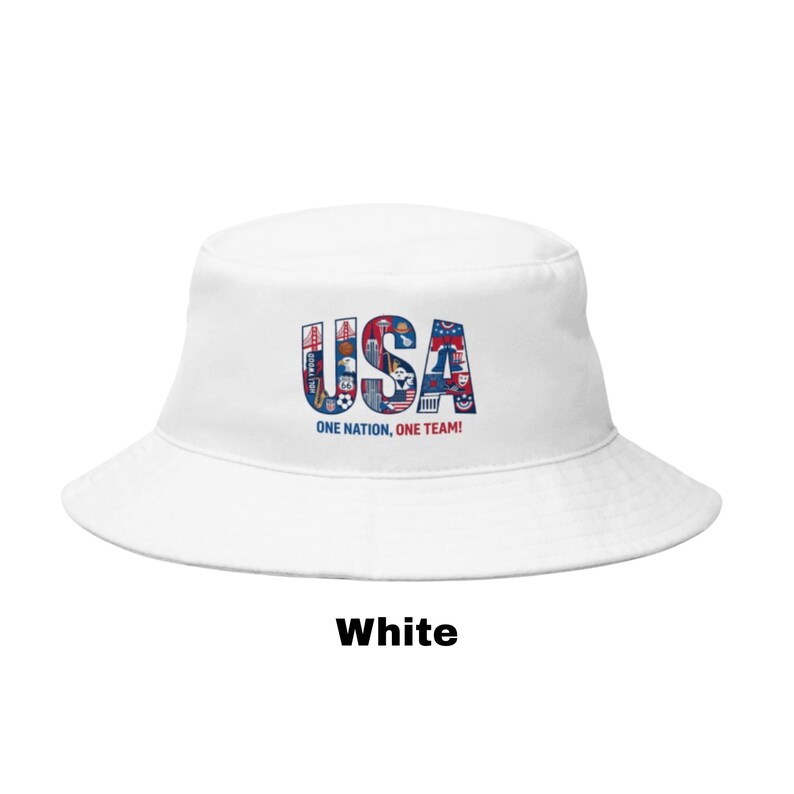 May include: White bucket hat featuring the word "USA" in red, white, and blue, with patriotic icons. The text "ONE NATION, ONE TEAM!" is below the word "USA". The word "White" is printed at the bottom of the image.