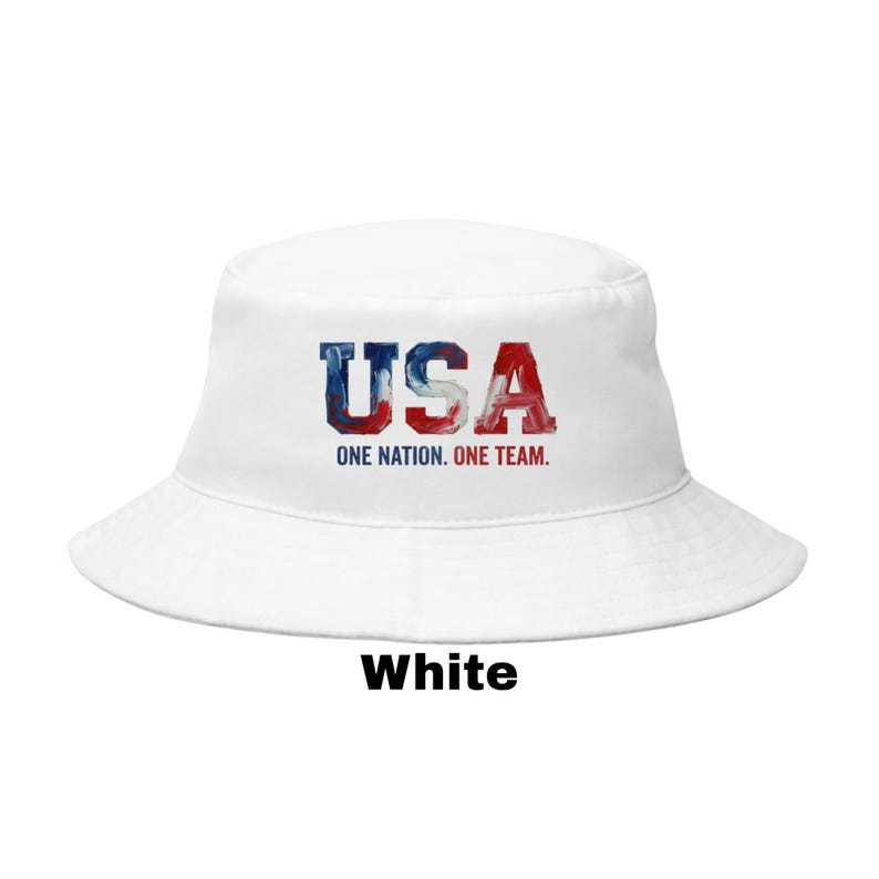 May include: White bucket hat featuring the word "USA" in red, white, and blue, with the text "ONE NATION. ONE TEAM." below. The word "White" is printed at the bottom of the hat.