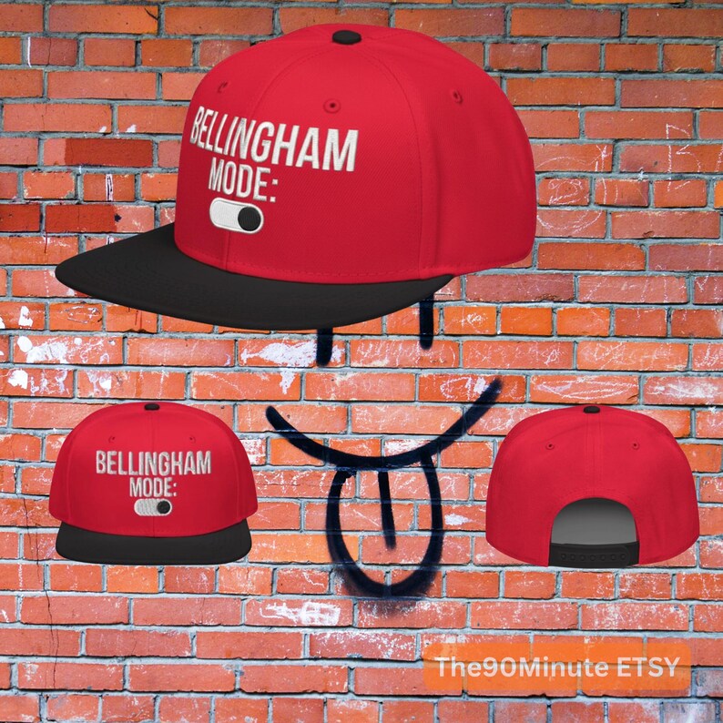 May include: A red and black snapback hat with the text "BELLINGHAM MODE:" in white. The hat has a black brim and a black button on top. The hat is displayed against a brick wall background.