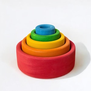 May include: A set of five nested circular wooden bowls in a rainbow colour gradient. The bowls are stacked from largest to smallest, featuring red, orange, yellow, green, and blue matte finishes. Each bowl has a smooth, flat base and open top.