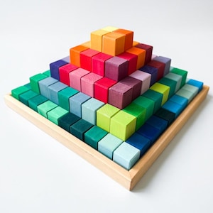 May include: A wooden pyramid toy made of colorful, square blocks. The blocks are arranged in a stepped pattern, with a variety of colors including green, blue, red, orange, and yellow. The toy sits on a light brown wooden tray.