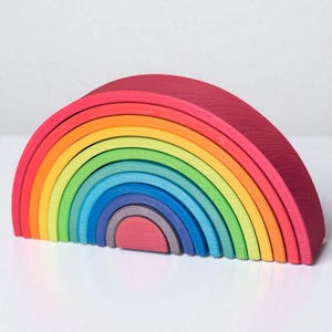 May include: A wooden rainbow stacker toy in a variety of colors. The toy is made of several arched pieces that nest together. The colors include red, orange, yellow, green, blue, and purple. The toy is designed for children.