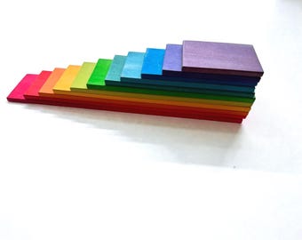 May include: A stack of colorful wooden blocks arranged in a rainbow gradient. The blocks are rectangular and vary in size, with the smallest at the bottom and the largest at the top. Colors include red, orange, yellow, green, blue, and purple.
