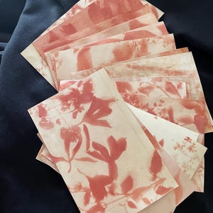 May include: A stack of rectangular paper cards featuring a botanical print in a muted terracotta orange color. Each card displays a unique silhouette of leaves and flowers against a light cream background, arranged in a fanned-out overlapping pattern.