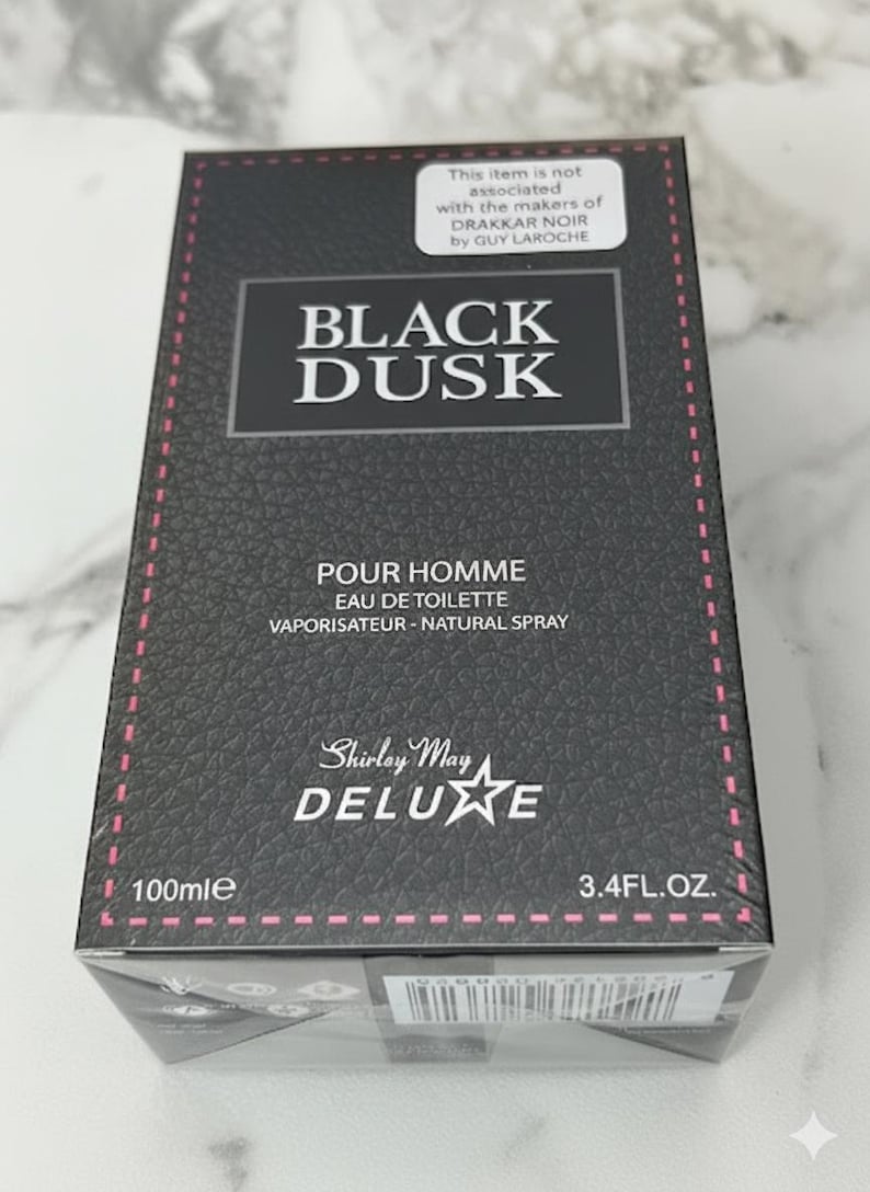 May include: Black Dusk Eau de Toilette spray for men. The box is black with a textured pattern and pink stitching. The text on the box includes "POUR HOMME", "EAU DE TOILETTE", and "Shirley May Deluxe". The bottle contains 3.4 fl oz (100ml).