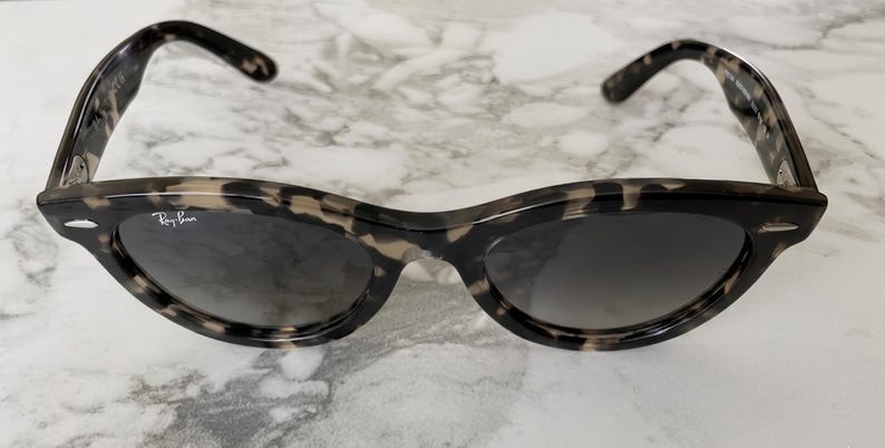 Puede incluir: Un par de gafas de sol Ray-Ban con un patr&oacute;n de carey. Las gafas de sol tienen una forma de ojo de gato cl&aacute;sica con lentes oscuras y el logotipo de Ray-Ban en blanco en la lente izquierda.