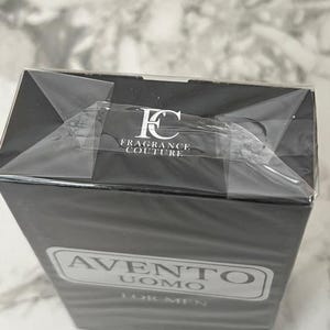 K&ouml;nnte beinhalten: Eine schwarze, rechteckige Schachtel mit "Avento Uomo For Men" Eau de Cologne. Die Schachtel ist in Klarsichtfolie verpackt und tr&auml;gt das Logo "FC FRAGRANCE COUTURE". Der Produktname befindet sich in einem wei&szlig;en, rechteckigen Rahmen.