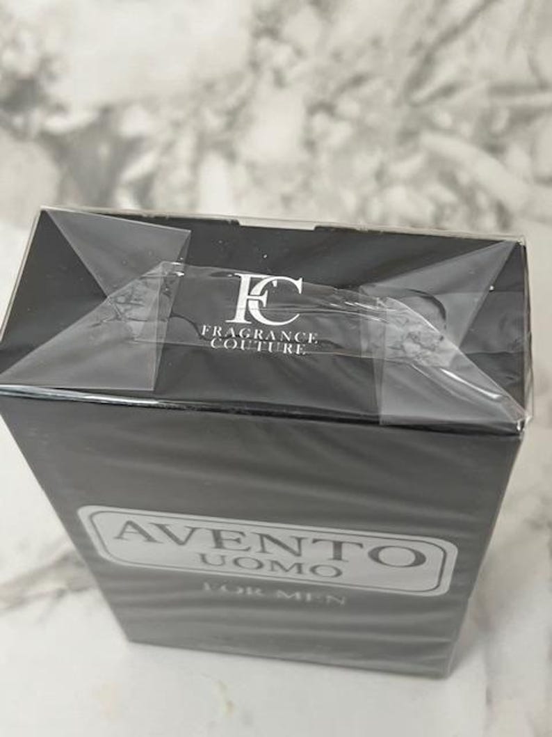 K&ouml;nnte beinhalten: Eine schwarze, rechteckige Schachtel mit "Avento Uomo For Men" Eau de Cologne. Die Schachtel ist in Klarsichtfolie verpackt und tr&auml;gt das Logo "FC FRAGRANCE COUTURE". Der Produktname befindet sich in einem wei&szlig;en, rechteckigen Rahmen.