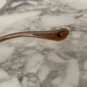 May include: A close-up of the arm of a pair of eyeglasses. The arm is a translucent brown color with glitter and a small "C" logo. The text "MADE IN CHINA" is printed on the arm.