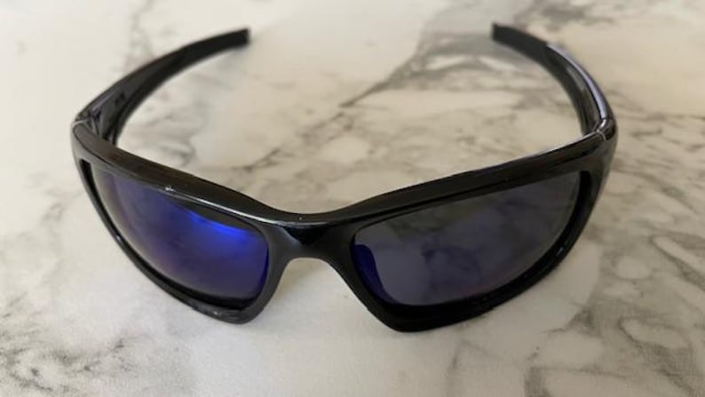 May include: Black sunglasses with a glossy finish and blue-tinted lenses. The sporty eyewear features a curved frame and a streamlined design, suitable for outdoor activities. The sunglasses are designed to provide eye protection from the sun.