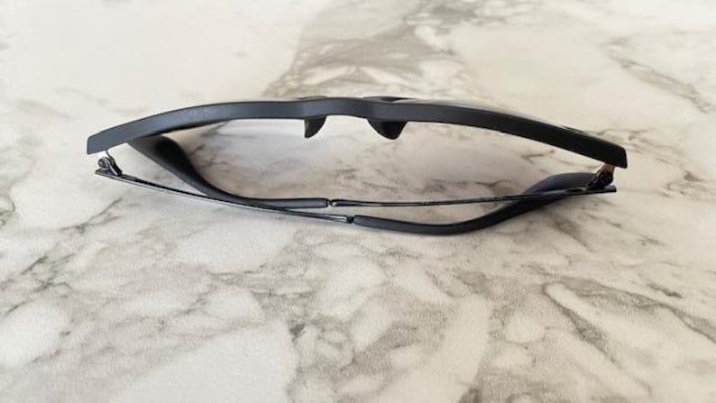 Puede incluir: Gafas con montura negra de dise&ntilde;o elegante y moderno. Las gafas est&aacute;n plegadas, mostrando las monturas oscuras y las varillas finas. Las lentes son transparentes y la est&eacute;tica general es minimalista y elegante.