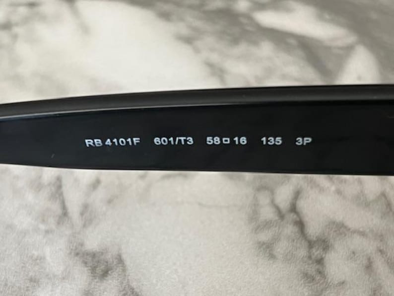 K&ouml;nnte beinhalten: Nahaufnahme des inneren Arms einer schwarzen Sonnenbrille. Der Text "RB 4101F 601/T3 58 16 135 3P" ist wei&szlig; auf dem schwarzen Arm aufgedruckt. Die Sonnenbrille scheint neu zu sein.