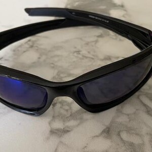 May include: Black sunglasses with blue-tinted lenses. The sunglasses have a sleek, modern design with a curved frame and a glossy finish. The lenses are rectangular and provide a contrast to the black frame.
