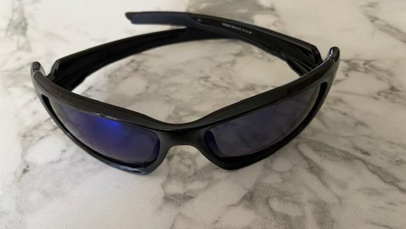 May include: Black sunglasses with blue-tinted lenses. The sunglasses have a sleek, modern design with a curved frame and a glossy finish. The lenses are rectangular and provide a contrast to the black frame.