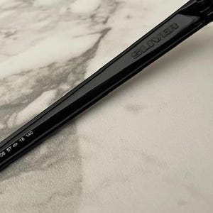 May include: Close-up of black sunglasses with a dark lens. The arm of the sunglasses has the brand name "SELIVER" printed on it. The arm also has the numbers "KL 009341-06 57 18 140" printed on it.