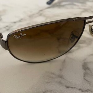 May include: Brown gradient lens sunglasses with a dark metal frame. The Ray-Ban logo is visible on the lens. The sunglasses have a classic aviator style.