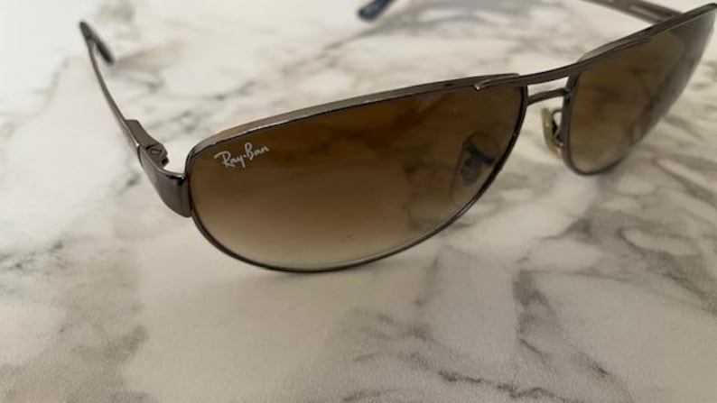 May include: Brown gradient lens sunglasses with a dark metal frame. The Ray-Ban logo is visible on the lens. The sunglasses have a classic aviator style.