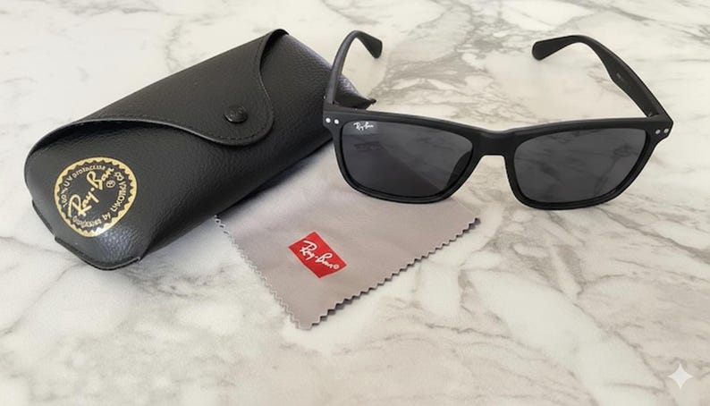 Pu&ograve; includere: Occhiali da sole neri con custodia e panno per la pulizia abbinati. Gli occhiali hanno una montatura rettangolare e lenti scure. La custodia &egrave; nera e il panno per la pulizia &egrave; grigio con un logo rosso. Un accessorio classico.