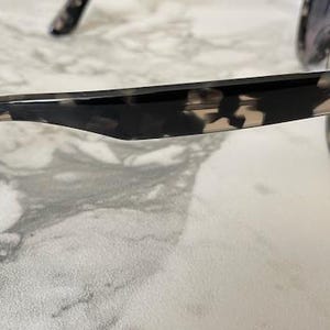 Puede incluir: Gafas de sol carey negras y marrones con lentes azules. El logotipo de Ray-Ban es visible en la patilla. Colocadas sobre una superficie de m&aacute;rmol blanco y gris.