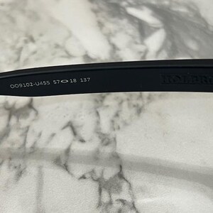 May include: Close-up of a black Holbrook sunglasses arm. The arm features the model number, lens and bridge measurements, and the brand name. The sunglasses are designed for eye protection.