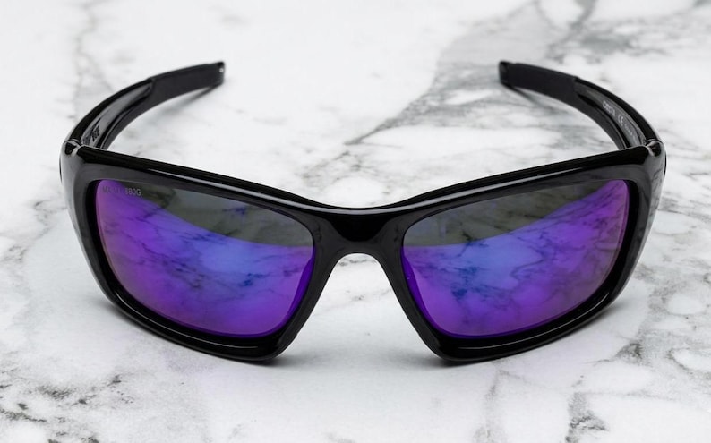 May include: Black sunglasses with purple and blue reflective lenses. The sunglasses have a rectangular frame and a glossy finish. The lenses reflect the surrounding environment, creating a vibrant color effect. The sunglasses are designed for eye protection.