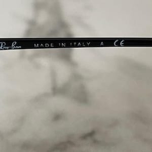 Puede incluir: Montura de gafas negra con el logotipo de Ray-Ban y el texto "MADE IN ITALY" y "CE". La montura es elegante y moderna, adecuada para lentes graduadas o gafas de sol.