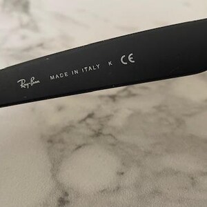 May include: Close-up of a black Ray-Ban sunglass arm. The text "MADE IN ITALY" and the Ray-Ban logo are visible. The arm also has a "K" and "CE" marking.