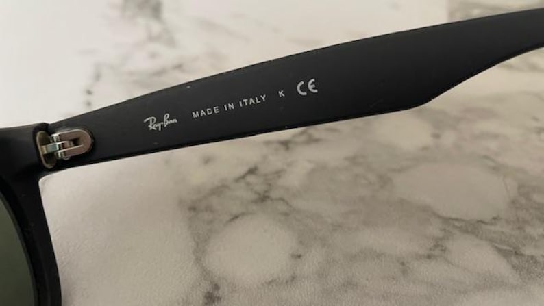 May include: Close-up of a black Ray-Ban sunglass arm. The text "MADE IN ITALY" and the Ray-Ban logo are visible. The arm also has a "K" and "CE" marking.