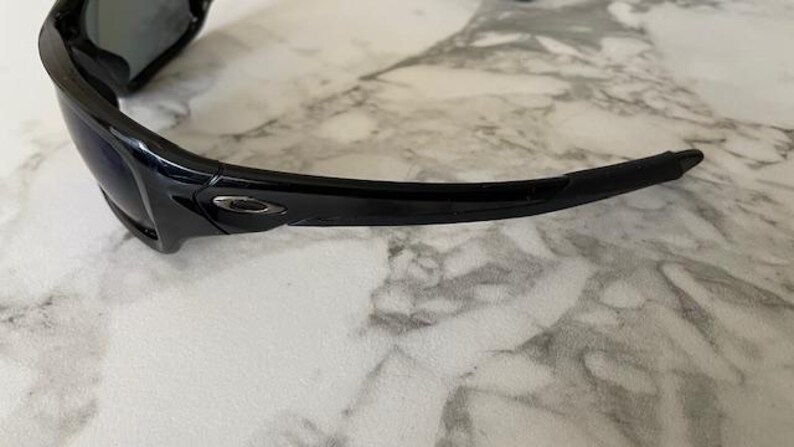 May include: Black sunglasses with a glossy finish. The sunglasses have a curved design with a dark lens and a sleek, modern aesthetic. The frame features a subtle logo detail.