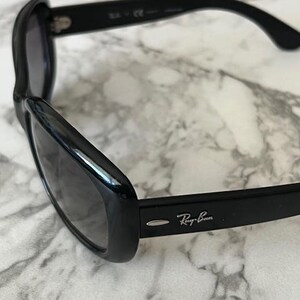 K&ouml;nnte beinhalten: Schwarze Sonnenbrille mit dunklen Gl&auml;sern. Das Ray-Ban-Logo ist auf dem B&uuml;gel sichtbar. Die Sonnenbrille hat ein schlankes, geschwungenes Design.
