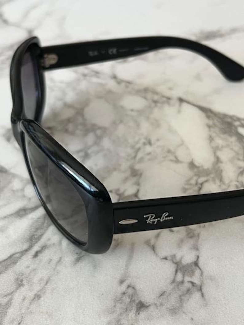 K&ouml;nnte beinhalten: Schwarze Sonnenbrille mit dunklen Gl&auml;sern. Das Ray-Ban-Logo ist auf dem B&uuml;gel sichtbar. Die Sonnenbrille hat ein schlankes, geschwungenes Design.