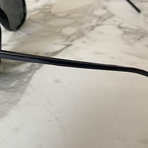 Puede incluir: Gafas de sol negras con lentes oscuras. El logotipo de Ray-Ban es visible en la patilla. Las gafas de sol est&aacute;n sobre un fondo de m&aacute;rmol.