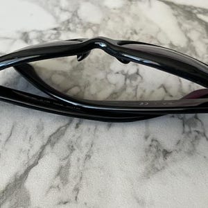 K&ouml;nnte beinhalten: Schwarze Sonnenbrille mit klassischem Rahmendesign. Die Sonnenbrille ist zusammengeklappt und zeigt die Innenseite des Rahmens und die Scharniere. Die Gl&auml;ser sind dunkel und der Rahmen gl&auml;nzend.