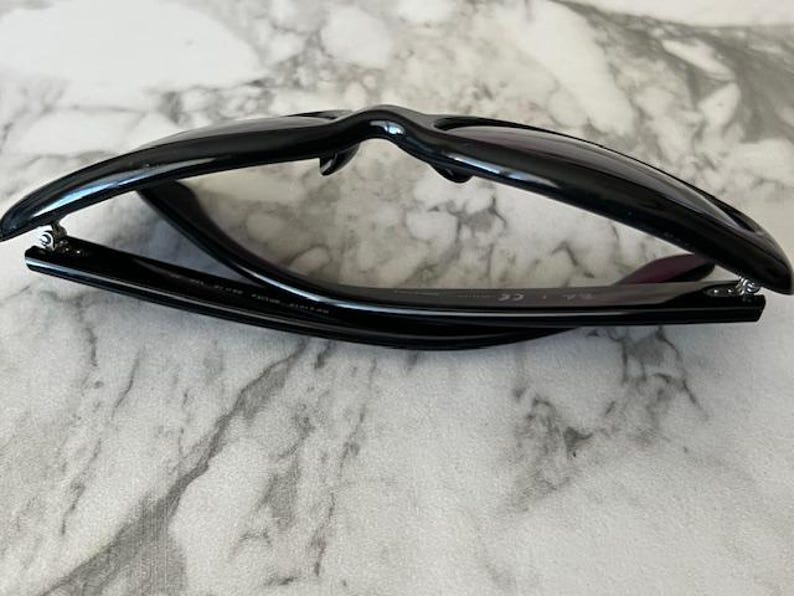 K&ouml;nnte beinhalten: Schwarze Sonnenbrille mit klassischem Rahmendesign. Die Sonnenbrille ist zusammengeklappt und zeigt die Innenseite des Rahmens und die Scharniere. Die Gl&auml;ser sind dunkel und der Rahmen gl&auml;nzend.