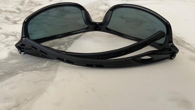 May include: Black sunglasses with dark lenses. The sunglasses have a sleek, modern design with a curved frame and temples. The lenses are a dark gray color, and the frame is glossy black.