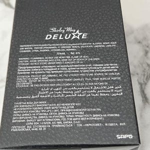 May include: Black box of Shirley May Deluxe perfume. The box has a textured surface and features the brand name in gold lettering. The ingredients and warnings are printed on the box.