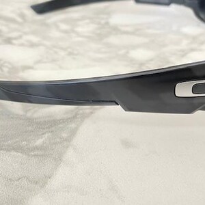 Puede incluir: Gafas de sol negras con un logotipo plateado en la patilla. Las lentes tienen un tinte amarillo y las monturas son negras. Las gafas de sol est&aacute;n dise&ntilde;adas para deportes o actividades al aire libre.
