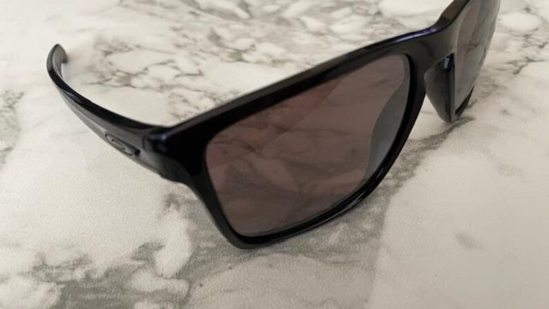 May include: Black sunglasses with dark tinted lenses. The sunglasses have a rectangular frame and a sleek, modern design. The arms curve slightly for a comfortable fit. The lenses appear to be polarized, offering protection from the sun.