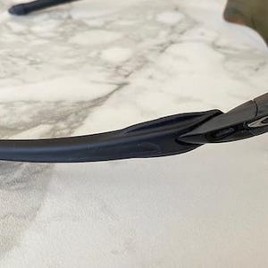 Peut inclure: Lunettes de soleil de sport noires avec des verres jaunes. Les lunettes ont un design &eacute;l&eacute;gant et moderne avec une monture et des branches noires. Le logo Oakley est visible sur le c&ocirc;t&eacute; de la monture. Les verres sont incurv&eacute;s.