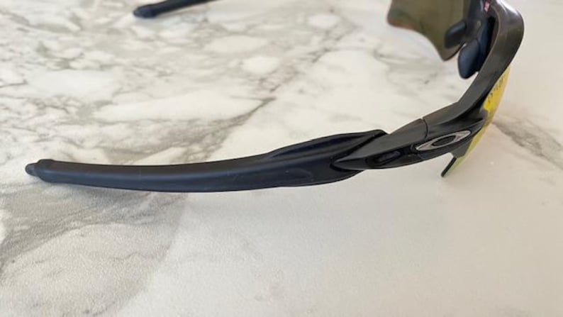Peut inclure: Lunettes de soleil de sport noires avec des verres jaunes. Les lunettes ont un design &eacute;l&eacute;gant et moderne avec une monture et des branches noires. Le logo Oakley est visible sur le c&ocirc;t&eacute; de la monture. Les verres sont incurv&eacute;s.